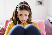 Mädchen liegt auf ihrem Bett und schaut auf ein Tablet und trägt Kopfhörer — Stockfoto