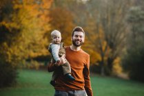 Vater und Sohn lächeln an einem Herbsttag im Park und tragen Erdtöne — Stockfoto