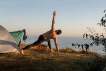Дорослий чоловік робить фізичні вправи на сході сонця, перед наметом — стокове фото