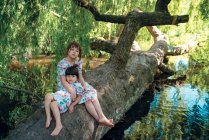 Портрет двох сестер, що сидять на дереві під озером — стокове фото