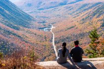 Hiking couple sitting on mountain ledge looking out over valley in NH. — Stock Photo