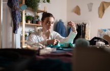 Young casual lady working on small business of dressmaking and sewing fabric pieces with needle in home studio — Stock Photo