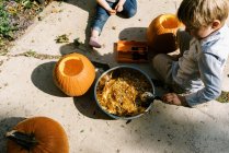 Dos niños tallando calabazas para Halloween en su patio - foto de stock