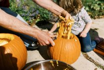 Маленькая девочка вырезает тыквы на Хэллоуин со своим отцом — стоковое фото