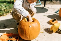 Ребенок вырезает тыквы на Хэллоуин в своем патио — стоковое фото