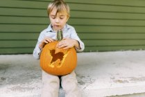 Kleiner Junge sitzt auf seiner Veranda und zeigt geschnitzten Halloween-Kürbis — Stockfoto