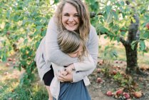 Una madre che abbraccia sua figlia con degli alberi di mele sul retro — Foto stock