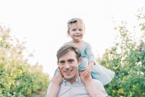 Um jovem pai com sua filha criança em seus ombros — Fotografia de Stock