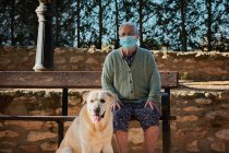 Avó com seu animal de estimação está sentado em um banco com sua máscara em — Fotografia de Stock