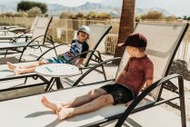 Vista da vicino dei giovani fratelli sulle sedie a bordo piscina che ridono insieme — Foto stock