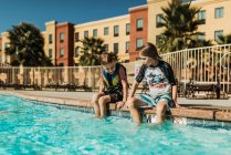 Young brothers sitting next to each other poolside on vacation — Stock Photo