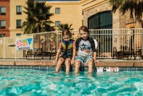 Jovens irmãos sentados ao lado uns dos outros à beira da piscina de férias — Fotografia de Stock
