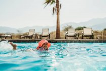 Вид сбоку маленькой девочки в розовой шляпе, плавающей в бассейне — стоковое фото