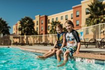 Young brothers sitting next to each other poolside on vacation — Stock Photo