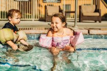 Vista frontal de los hermanos jóvenes jugando en la piscina de vacaciones en California - foto de stock