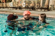 Забавный образ отца в детской шляпе, играющего в бассейне с сыновьями — стоковое фото