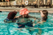 Imagen divertida de papá en sombrero de niño jugando en la piscina con hijos - foto de stock