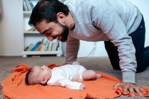 Smiling dad with beard playing with infant daughter on orange blanket — Stock Photo