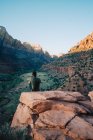 Черный человек, сидящий на скале и созерцающий гору на закате — стоковое фото