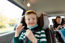 Мальчик начального возраста улыбается, сидя в машине в маске — стоковое фото