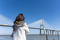 Rückansicht einer Frau, die am Flussufer steht und zur Flussbrücke blickt — Stockfoto