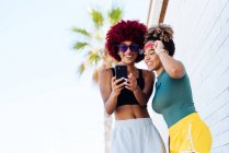 Zwei lateinamerikanische Frauen mit Afro-Haaren schauen aufs Smartphone — Stockfoto