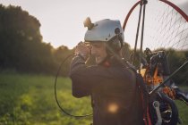 Young man, with the Powered Paragliding engine in his shoulders, gets ready to fly, at sunset time, pulling the rope to start the engine. — Stock Photo