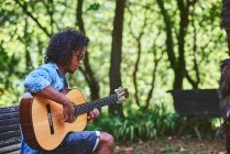 Musicista che suona la chitarra in un bel parco. E 'circondato dalla vegetazione. — Foto stock