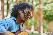 Musician playing guitar in a nice park. He is surrounded by vegetation. — Stock Photo