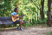 Musiker spielt Gitarre in einem schönen Park. er ist von Vegetation umgeben. — Stockfoto