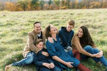 Eine glückliche fünfköpfige Familie sitzt zusammen auf einem Feld — Stockfoto