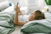 Kleiner Junge wacht morgens auf und spielt mit seinem Tablet — Stockfoto