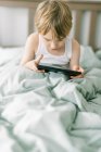 Kleiner Junge wacht morgens auf und spielt mit seinem Tablet — Stockfoto