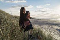 Madre e hija de pie en la playa contra la vista del paisaje marino - foto de stock