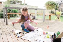 Молода дівчина малює зовні на дерев'яній палубі з кішкою на фоні — стокове фото