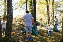 Gruppe ehrenamtlicher Familien sammelt an sonnigem Tag Müll im Wald — Stockfoto