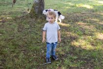 Niño mirando a la cámara en un parque natural con un perro - foto de stock