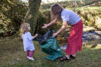 Ehrenamtliche Mutter mit ihrer Tochter, die einen Müllsack am Fluss hält — Stockfoto