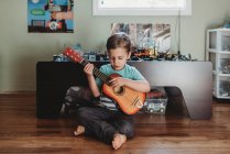 5 yr old boy sitting on hardwood floor playing guitar — Stock Photo