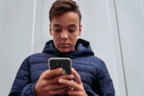Adolescente com telefone celular em uma parede branca — Fotografia de Stock