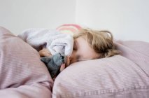 Menina dormindo em sua cama abraçando seus brinquedos e cobertor em casa — Fotografia de Stock
