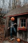 Hombre con cabeza de calabaza tallada de miedo en cobertizo con hacha para Halloween. - foto de stock