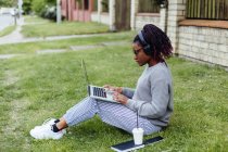 Estudiante afroamericano usando laptop y escuchando música en la calle - foto de stock