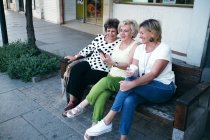 Frauen sitzen fröhlich lächelnd auf einer Bank und zeigen ihr Handy. — Stockfoto