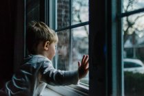 Un bambino guarda fuori da una finestra. — Foto stock