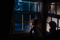 Un bambino guarda fuori da una finestra verso il sole. — Foto stock