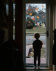 Маленький хлопчик дивиться скляні штормові двері з осіннім листям на i — стокове фото