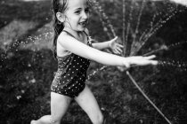 Ein kleines Mädchen spielt im Sprinkler. — Stockfoto