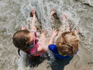 Un niño y una niña se sientan en el surf en la playa. - foto de stock