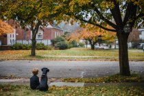 Ein kleiner Junge und sein Welpe sitzen auf dem Gras und betrachten die Blätter. — Stockfoto